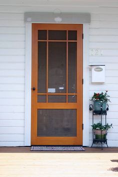 the front door of a white house with potted plants on the porch and an open screen door