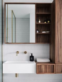 a white sink sitting under a bathroom mirror next to a wooden shelf filled with bottles