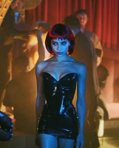 a woman with red hair and black latex is standing in front of a group of people