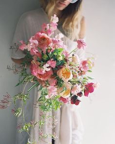 a woman standing next to a wall holding a bouquet of pink and orange flowers in her hands