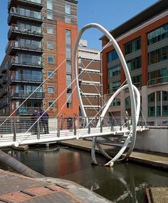 a pedestrian bridge over a river with buildings in the background