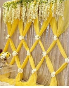 a yellow and white wedding backdrop with flowers on the top, along with sheer drapes