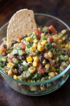 a glass bowl filled with corn, black beans and guacamole next to a tortilla chip