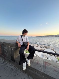 a man sitting on a ledge next to the ocean with food in his hand and looking at the water