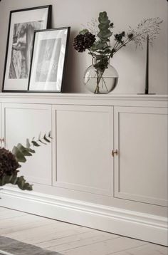 a vase with flowers sitting on top of a white cabinet next to two framed pictures