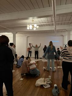 several people standing and sitting on the floor in an empty room with their hands up