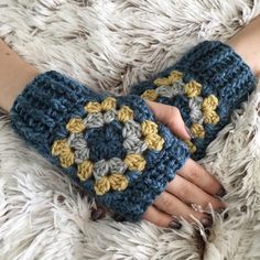 a woman's hand is holding a crocheted blue and yellow mitt