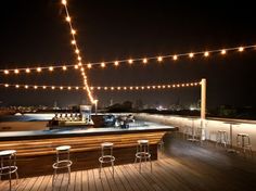 an outdoor bar is lit up at night with string lights strung across the roof top