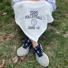 a young child sitting in the grass with a volleyball bib over his leg and shoes