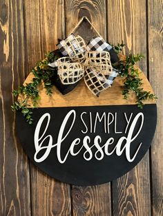 a black and white sign that says simply blessed hanging on a wooden wall with greenery