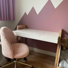 a pink chair sitting next to a desk in a room with mountains painted on the wall