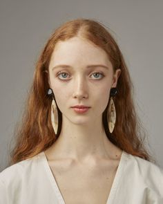 a woman with long red hair wearing large earrings and a white shirt is looking at the camera