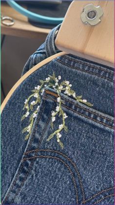 the back pocket of a pair of jeans with white flowers on it and a wooden button