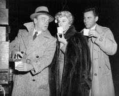 two men and a woman drinking from cups in front of a man wearing a coat