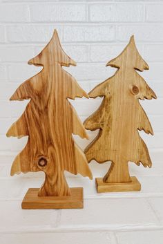 two wooden christmas trees sitting next to each other on top of a white brick wall