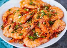 a white plate topped with cooked shrimp and garnished with scallions on a blue cloth