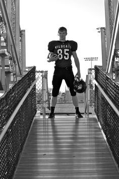 a black and white photo of a football player standing on a bridge holding a ball