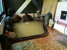 a bath room with a large tub filled with water next to rocks and a window