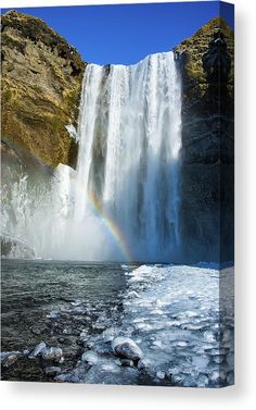 a rainbow in the sky over a waterfall with ice on the ground and water running down it