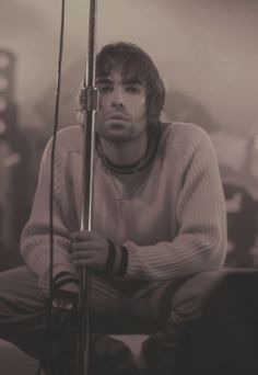 a man sitting in front of a microphone with his hands on the pole and looking at the camera