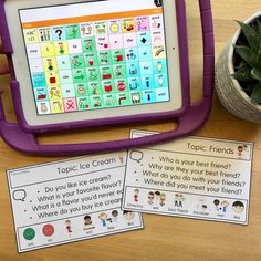 a tablet sitting on top of a wooden table next to a potted plant and two cards