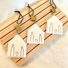 three small white houses are hanging from hooks on a wooden board with black string attached to them