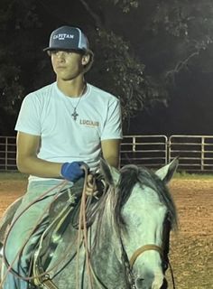 a man riding on the back of a white horse in a fenced area at night