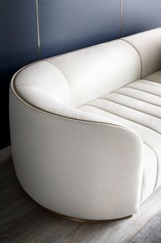 a white leather couch sitting on top of a hard wood floor next to a blue wall