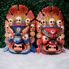 two colorful masks sitting next to each other on top of a white fur covered ground