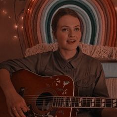 a woman sitting on a couch holding a guitar in front of a wall with lights