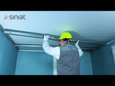 a man wearing a hard hat and overalls is fixing the ceiling in a room