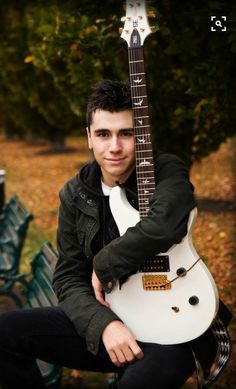 a man sitting on a park bench holding an electric guitar