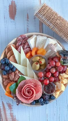 a wooden platter filled with cheese, fruit and crackers