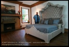 a man standing next to a large bed in a room with wood floors and white walls