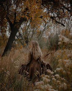 a woman sitting in tall grass with her back to the camera, looking at trees