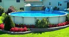 an above ground pool surrounded by flowers and shrubs in the backyard with a water fountain