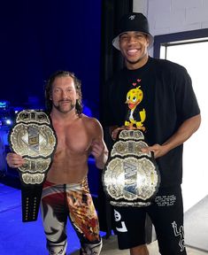 two men standing next to each other holding wrestling belts