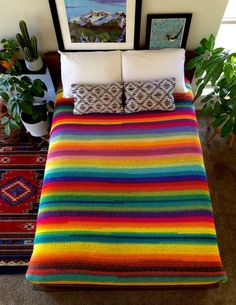 a bed covered in multi colored blankets and pillows