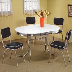 a white table with four chairs and a flower vase on top of it in a room