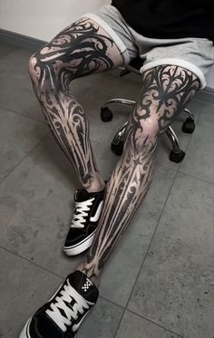 a man sitting on top of a chair covered in black and white tattoos with his legs crossed