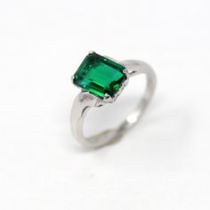 Beautiful vintage circa 1950s 10k white gold and simulated emerald ring! This lovely bypass style ring features a rectangular faceted dark green hued stone that is set in a four prong setting. The setting remains unadorned with a pretty polished finish. A fabulous piece of Mid Century era jewelry, featuring May's birthstone color! *Sale - price reduced from $250 USD to $230 USD.  ERA - Circa 1950s - Mid Century METAL / MATERIAL - 10k white gold, simulated emerald stone (faceted green glass). MARKINGS / HISTORY - Inside of band is marked with what looks like 'HART 10K'  CONDITION - Good vintage condition. Ring has been refurbished, polished, cleaned, and newly rhodium plated by our jeweler. Very little wear remains to metal. Simulated emerald stone is secure in setting. Light age consistent Smaragd Ring, Birthstone Colors, Logo Gifts, Emerald Stone, Metal Material, Emerald Ring, Sale Price, Green Glass, Rings Statement