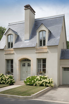 a house with white flowers in the front yard and two garages on each side