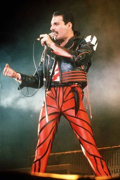 a man in red and black outfit on stage holding a microphone with his right hand