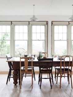 a dining room table and chairs with windows in the background