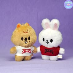 two stuffed animals that are standing next to each other on a purple background, one is wearing a red shirt and the other has a white bunny