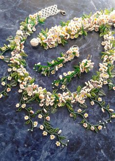 a necklace with white flowers and green leaves on a blue marble surface, next to a silver chain