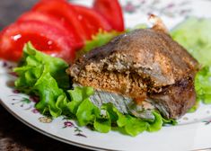 a white plate topped with meat and lettuce next to tomato wedges on top of a table