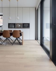 a dining room table with chairs and lights hanging from it's ceiling over the kitchen