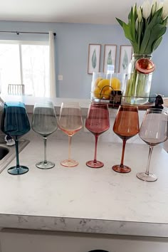 four wine glasses sitting on top of a kitchen counter next to a vase filled with flowers