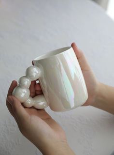 a person holding a white coffee cup with pearls on it